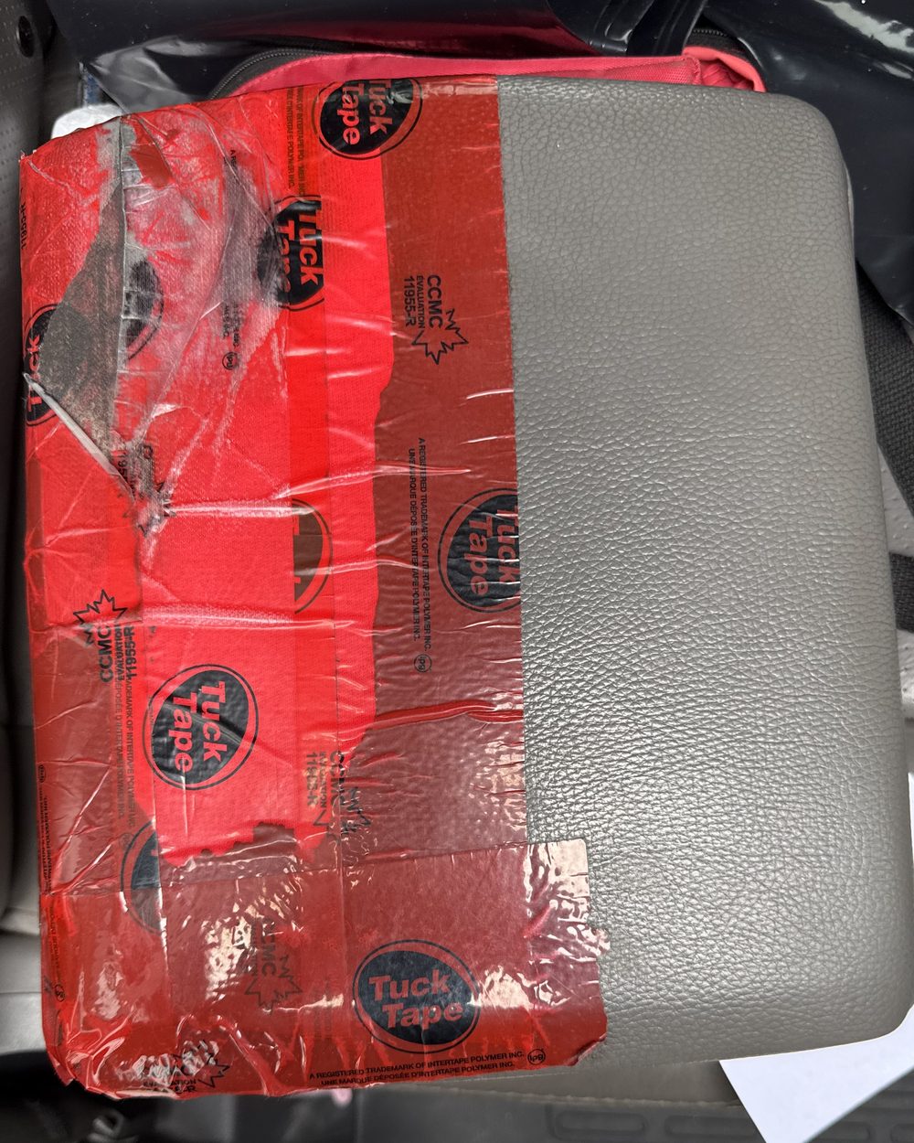 Honda Ridgeline centre console lid sitting on a truck seat. The cover has split across the lower half and is wrapped in red tape.