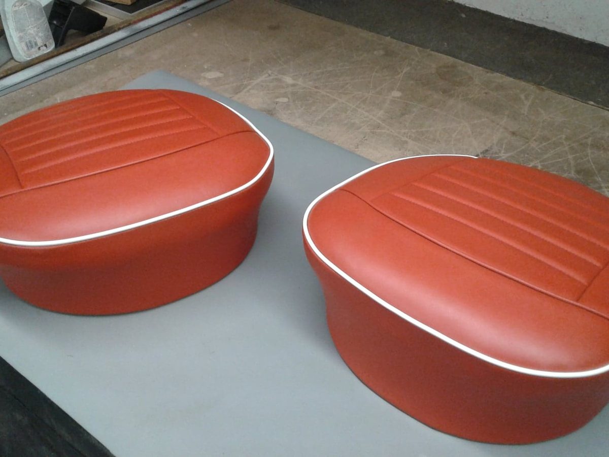 Two round seat pads recovered in red vinyl with white piping around the edge.